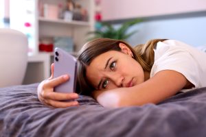 counselling for teens:Depressed Teenage Girl Lying On Bed At Home Looking At Mobile Phone
